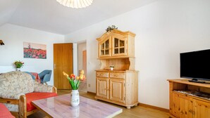 A living room with a sofa, a wooden cabinet, a television, and a vase with flowers. - Apartment '3' with Private Garden, Balcony and Wi-Fi (Hagnau am Bodensee)