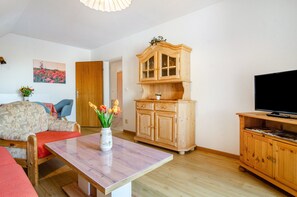 A living room with a sofa, a wooden cabinet, a television, and a vase with flowers.