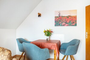 A dining area with a table, chairs, a vase with flowers, a wall-mounted light, and a poppy field painting.