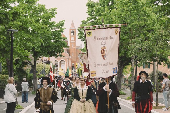 A historical reenactment parade with participants in period costumes, a church in the background, and a banner with text.
