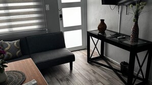 Una sala de estar moderna con un sofá, una mesa de centro, un televisor montado en la pared y una mesita auxiliar con un florero.