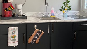 Una cocina con microondas, repisas con platos y tazas, un lavamanos y una planta en maceta.