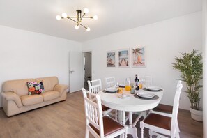 A dining area with a round table, white chairs, a beige sofa, and a ceiling light fixture. - Justo's House Apartment with Private Terrace, Wi-Fi and Air Conditioning (Faro)