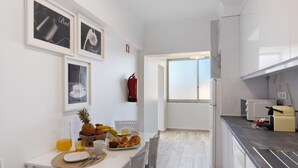 Una cocina moderna con armarios blancos, una mesa de comedor con desayuno servido y un ventanal que proporciona luz natural.
