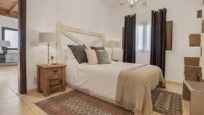 Un dormitorio con una cama de madera, dos mesitas de noche, una araña, un espejo grande y una pared de piedra.