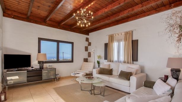 Una sala de estar con techo de madera, televisor de pantalla plana, un conjunto de sofá, una mesa de centro y un ventanal grande.