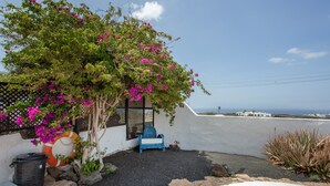 Un patio con una silla, un árbol de flores rosas y vista al océano.