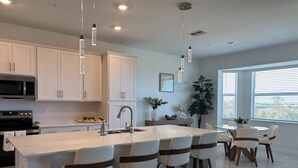 A modern kitchen with white cabinets, stainless steel appliances, and a central island with bar stools. - WELLEN GOLF & COUNTRY CLUB GATAWAY 
In a Modern Style 2 bd Condo (Venice)