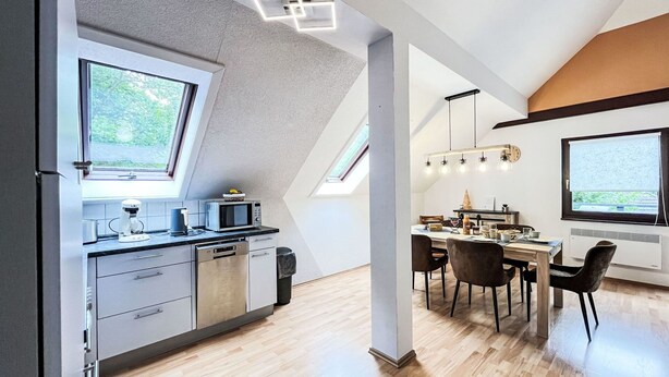 A modern kitchen with a dining area, featuring skylights, a built-in oven, and a dining table with chairs. - Cosy apartment in villa for 8 people with WIFI, TV, terrace and pets allowed (Bad Wildungen)