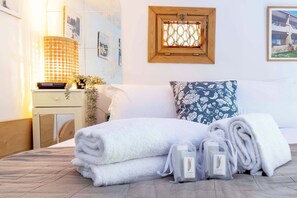 A neatly made bed with rolled white towels, a bedside table with a lamp, and a window with a wooden frame. - Italian Experience-Suite Vogel (Florence)