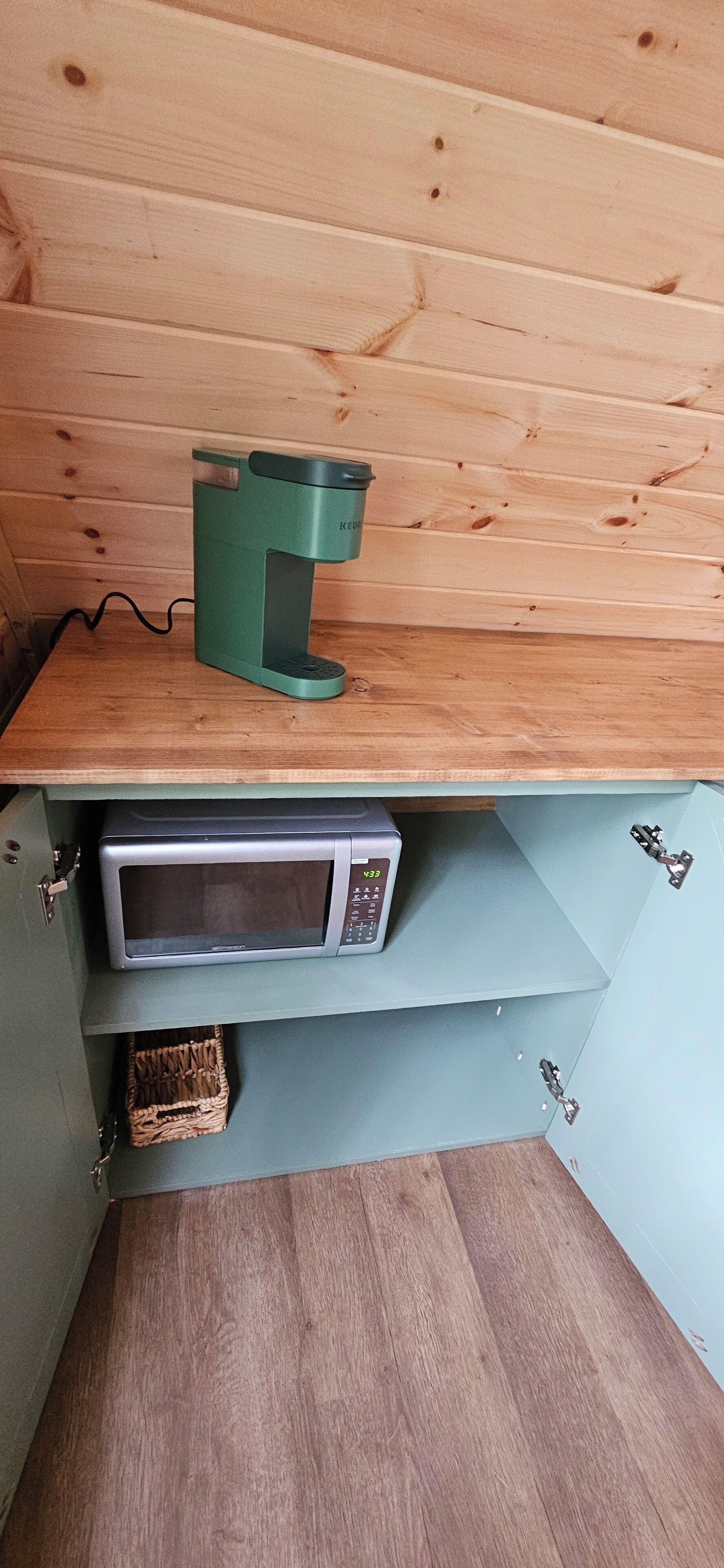 A kitchenette with a green coffee maker and a silver microwave on a wooden countertop.