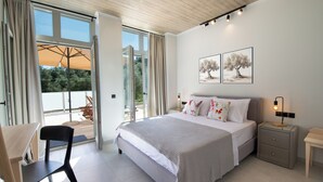 Een moderne slaapkamer met een groot bed, een bureau en een stoel. Er is een raam met gordijnen en uitzicht op groen buiten.