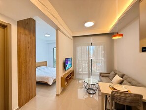 Una sala de estar moderna con un sofá, una mesa de comedor con sillas, un televisor montado en la pared y un ventanal con vistas a la ciudad.