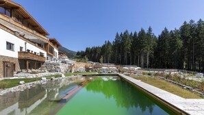 A modern building with a stone facade, a swimming pool, and a forested mountain backdrop. - Chalet in Neukirchen by the Slopes (Neukirchen am Grossvenediger)