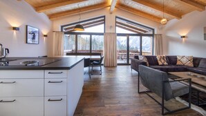 A spacious living area with a wooden ceiling, a sofa, a coffee table, and a kitchen area with a counter and cabinets. - Chalet in Neukirchen by the Slopes (Neukirchen am Grossvenediger)