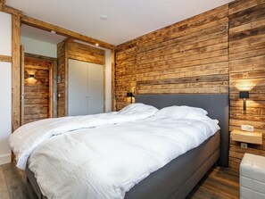 Relax in this stylish bedroom with a large bed, wooden paneling, and wall-mounted lighting.
