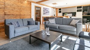 Moderni olohuone, jossa on kaksi harmaata sohvaa, sohvapöytä ja katossa näkyvät puupalkit.