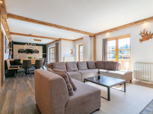 A modern living room with a sectional sofa, a coffee table, and a dining area with chairs and a kitchen in the background.