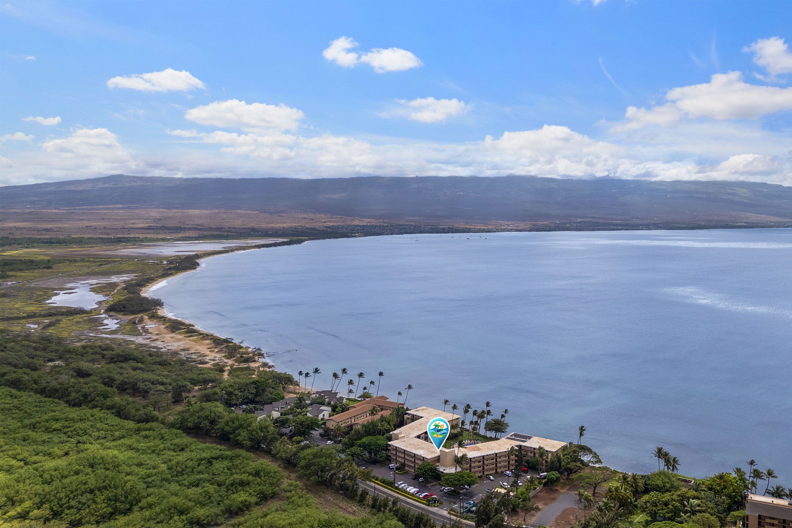Ein Küstenresort mit Blick auf den Strand, einschließlich eines großen Mehrstöckengebäudes und einem Parkplatz.
