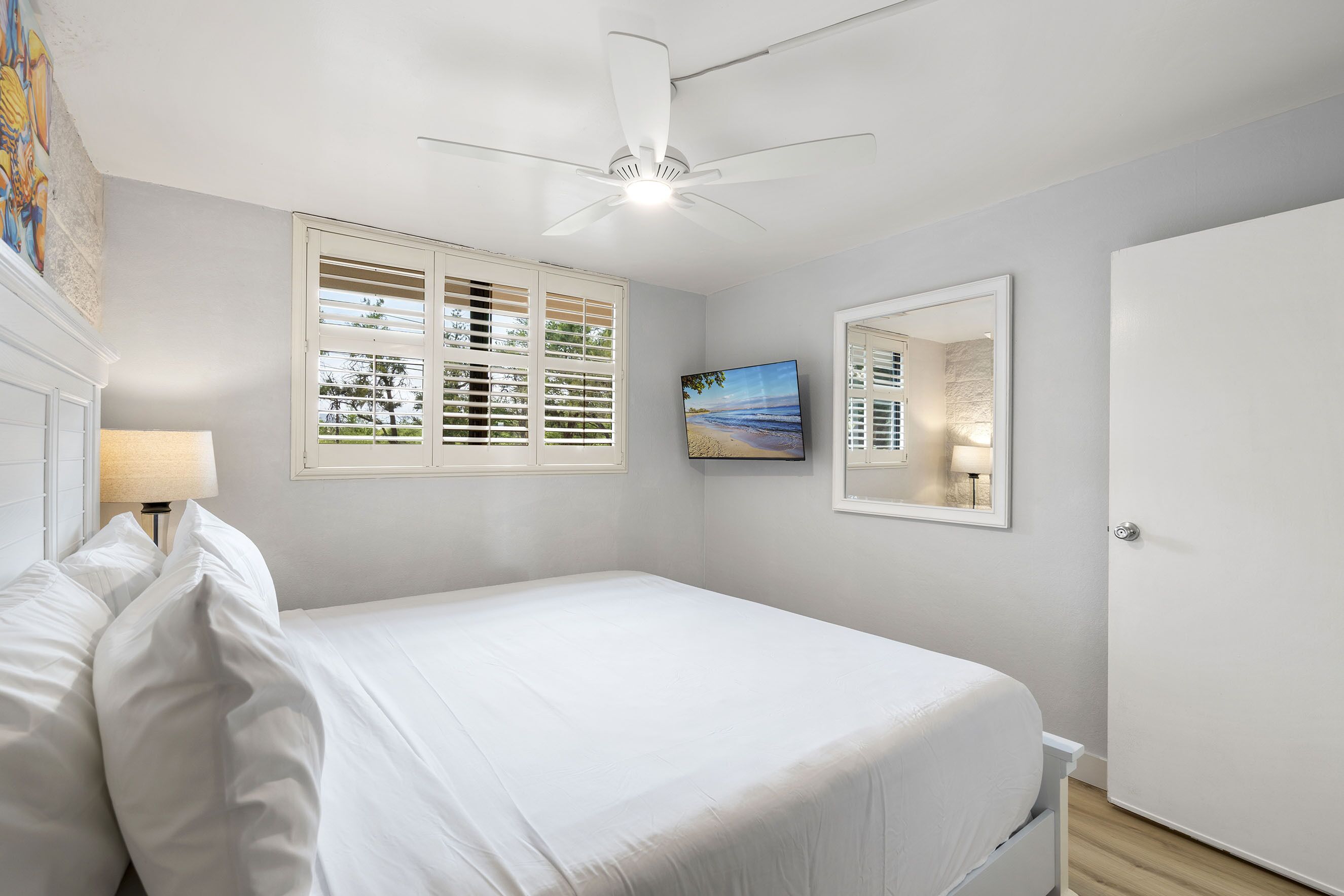 A bedroom with a bed, a ceiling fan, a window with blinds, a painting, and a door.