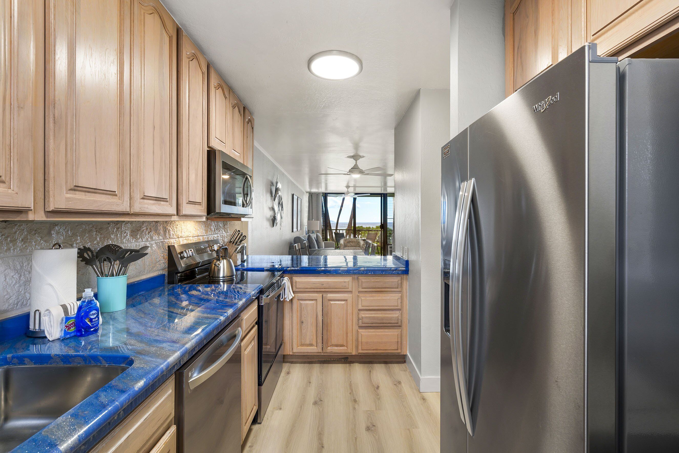 A kitchen with wooden cabinets, a stainless steel refrigerator, a blue marble countertop, and a ceiling fan.