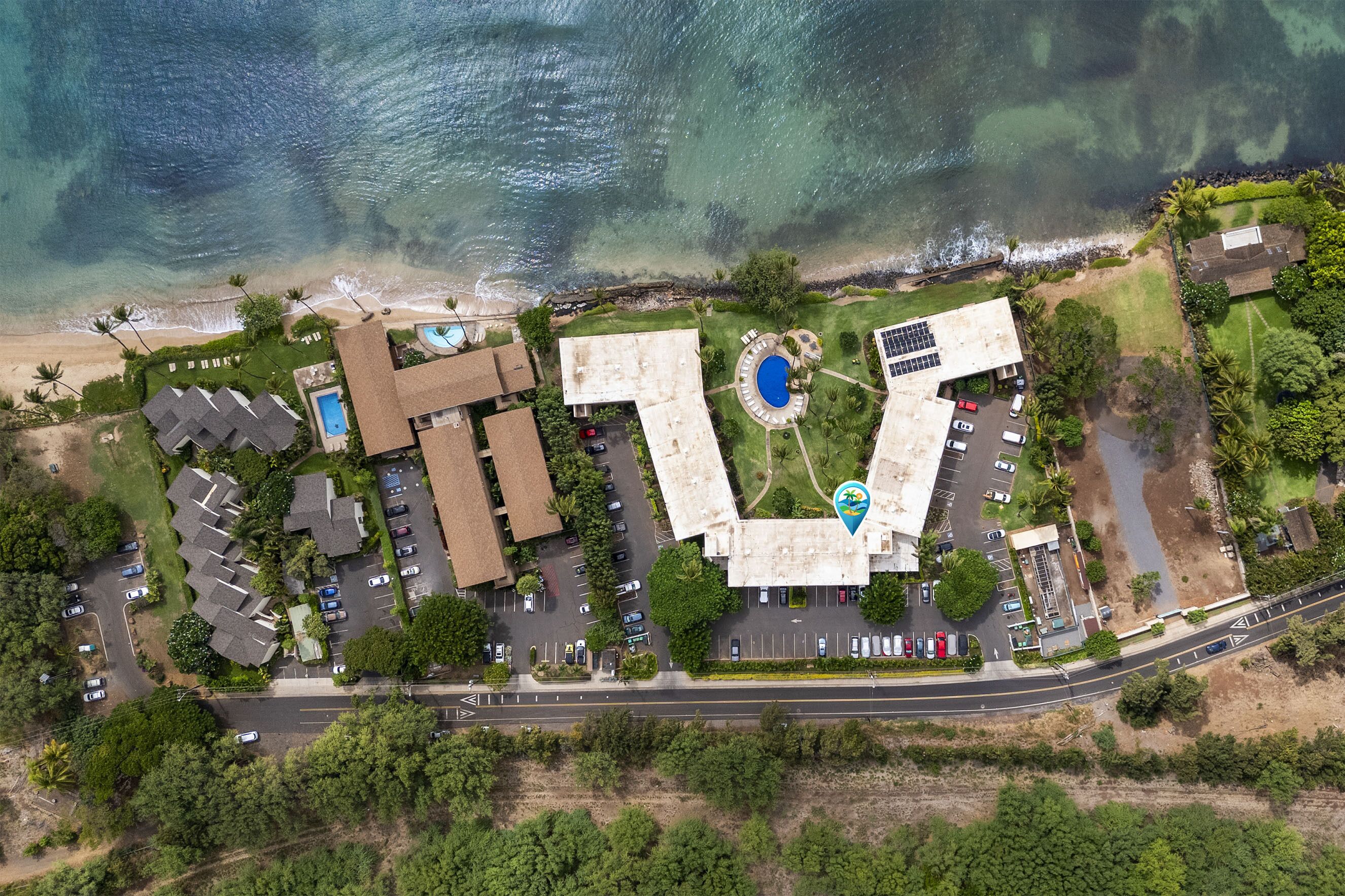An aerial view of a coastal property with multiple buildings, a swimming pool, and a road.