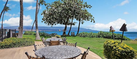 Un patio con una mesa redonda y sillas, rodeado de palmeras y vista al océano.