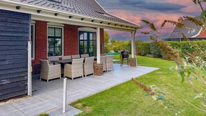 Ein Haus mit überdachter Terrasse, Gartenmöbeln und Blick auf den Garten.