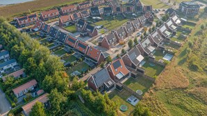 Luftaufnahme eines Wohngebiets mit Häusern, die Satteldächer und Solaranlagen haben, umgeben von viel Grün und einem Gewässer.