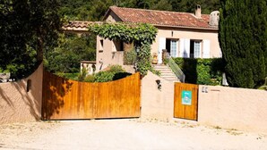 A house with a wooden gate, a staircase leading to the entrance, and a lush green hillside in the background. - Gîte 8 pers air-conditioned, 3 bedrooms with bathrooms, private pool. Peaceful (Évenos)