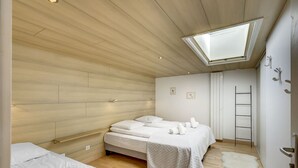 A modern bedroom with a skylight, wooden walls, a bed with white linens, a small bedside table, and a white rug.