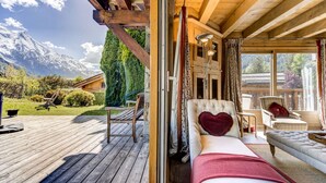 A cozy cabin with a wooden deck, a plush sofa, and a view of snow-capped mountains.