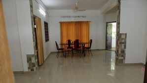 Une pièce spacieuse comprenant une table et des chaises, un ventilateur de plafond et une fenêtre avec des rideaux.