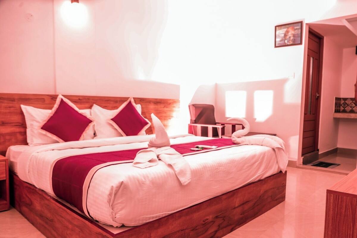 Een net opgemaakt bed met een houten hoofdbord, een rode plaid en kussens in een hotelkamer.