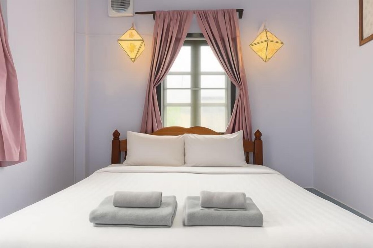 A neatly made bed with white linens and two folded towels, a wooden headboard, and two wall-mounted lamps.