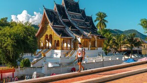 A traditional Thai temple with ornate architecture, a staircase leading to the entrance, and a clear view of the surrounding greenery and hills.