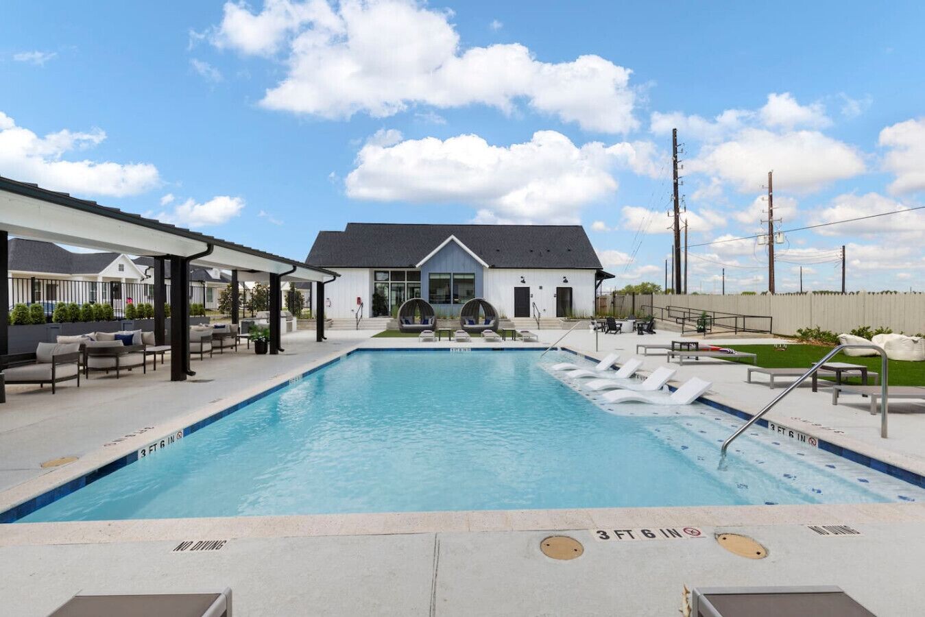 A swimming pool with lounge chairs and a covered seating area, surrounded by a building with a grey roof and a white exterior.