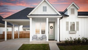 A white single-story house with a front porch, a garage, and a small attached shed. - Modern Magnolia Cottage | Pool & Gym Access (Magnolia)