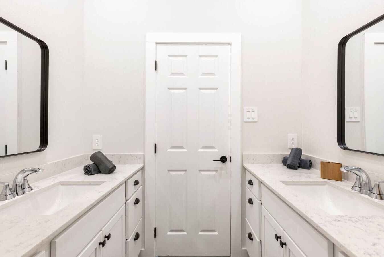 A bathroom with two sinks, a white door, and a mirror on each side.