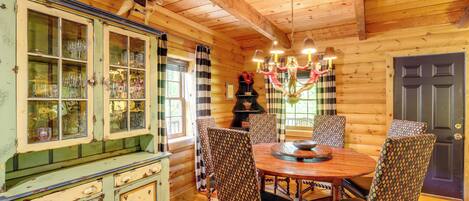 A wooden cabin interior with a dining table, chairs, and a cabinet with glass doors.