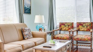 A living room with a beige sofa, a wooden coffee table, a floral armchair, and a wooden chair. - Walk to Gold Beach: Charming Cottage w/ Yard! (Gold Beach)