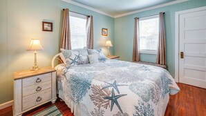 A bedroom with a bed, nightstands, lamps, and a door. - Walk to Gold Beach: Charming Cottage w/ Yard! (Gold Beach)