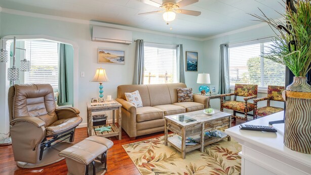 A living room with a recliner, sofa, coffee table, and chairs. There is a ceiling fan, a window with curtains, and a vase with plants. - Walk to Gold Beach: Charming Cottage w/ Yard! (Gold Beach)