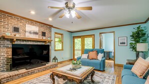 A living room with a brick fireplace, a ceiling fan, a blue sofa, and a large flat-screen TV.