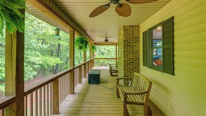 A covered porch with wooden railings, a ceiling fan, and a bench.