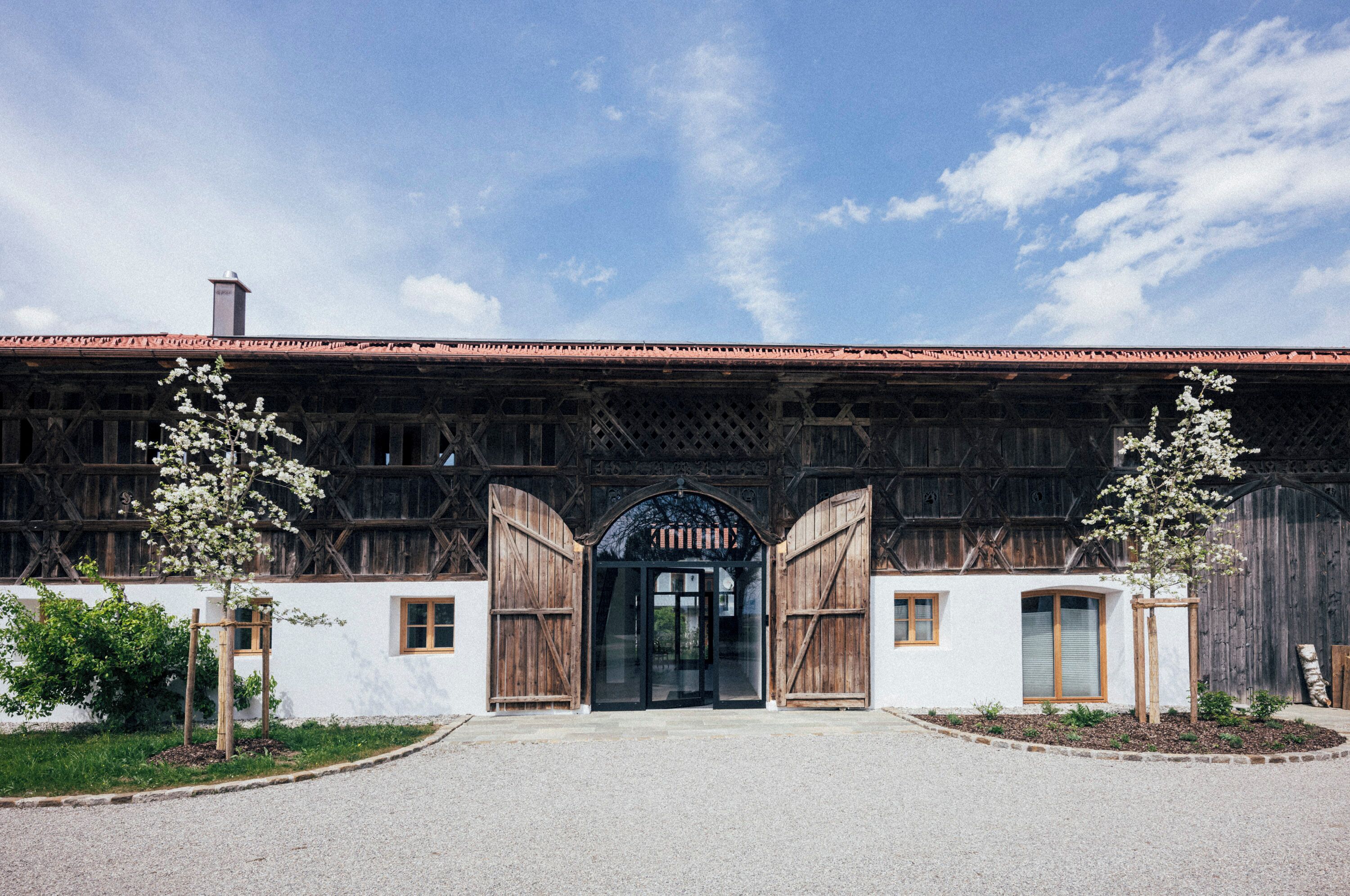 A traditional building with a wooden facade, a central arched entrance, and two trees in front.