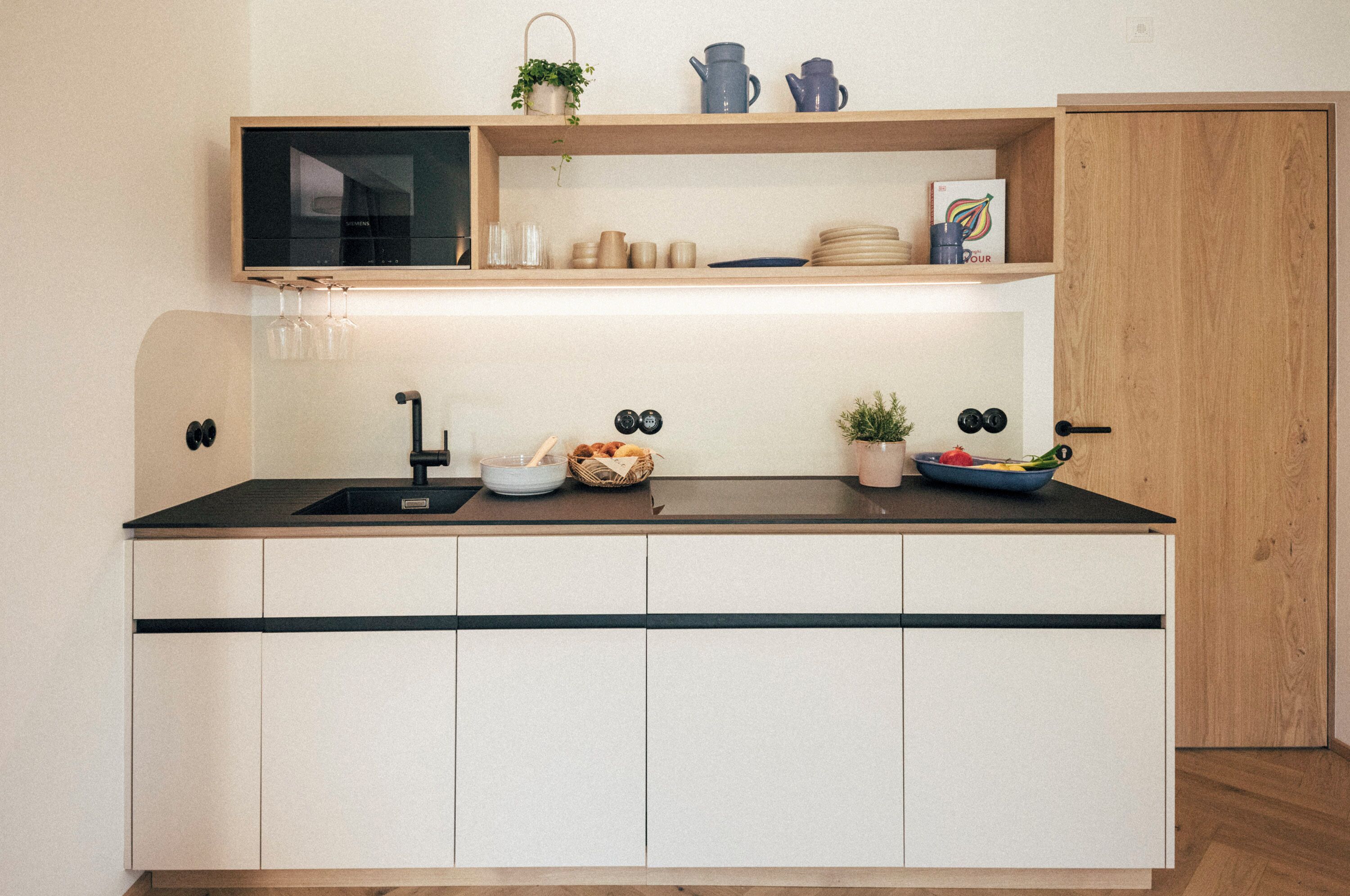 A compact kitchen with a black countertop, white cabinets, and a wooden door.