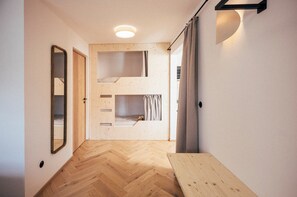 Un couloir doté d’un parquet en bois disposé en chevrons, d’un banc en bois, d’un miroir et d’une porte avec une petite fenêtre.