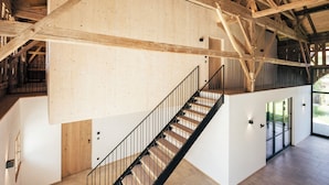 Un intérieur spacieux avec un escalier en bois, de hauts plafonds et une vue sur l’extérieur.