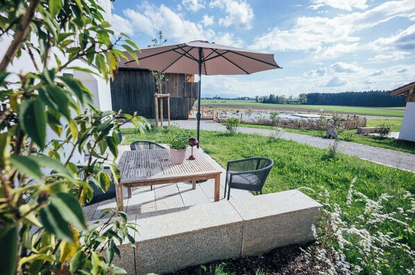 Une terrasse extérieure avec une table et des chaises, un banc en bois et un grand parasol.